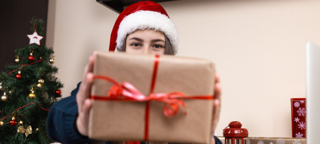 Girl in santa claus hat talks and gives a gift using laptop